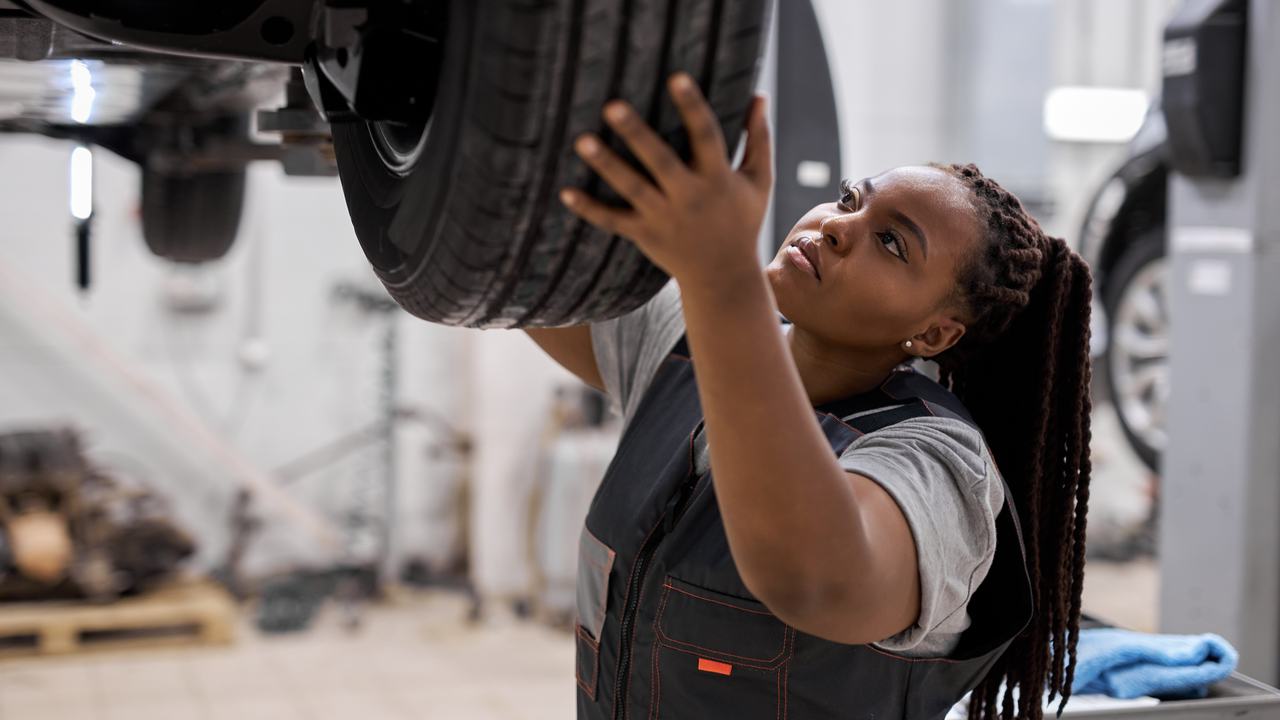 A technician checking the wheel and suspension of a car on a workshop lift