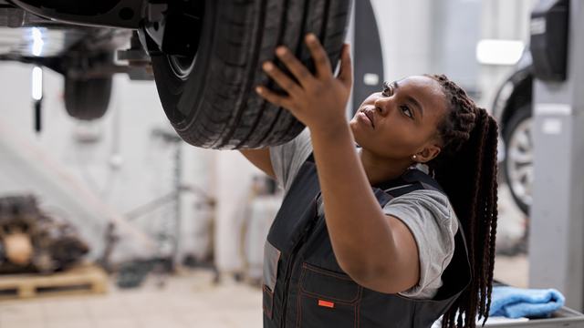 A technician checking a wheel and suspension on a raised vehicle